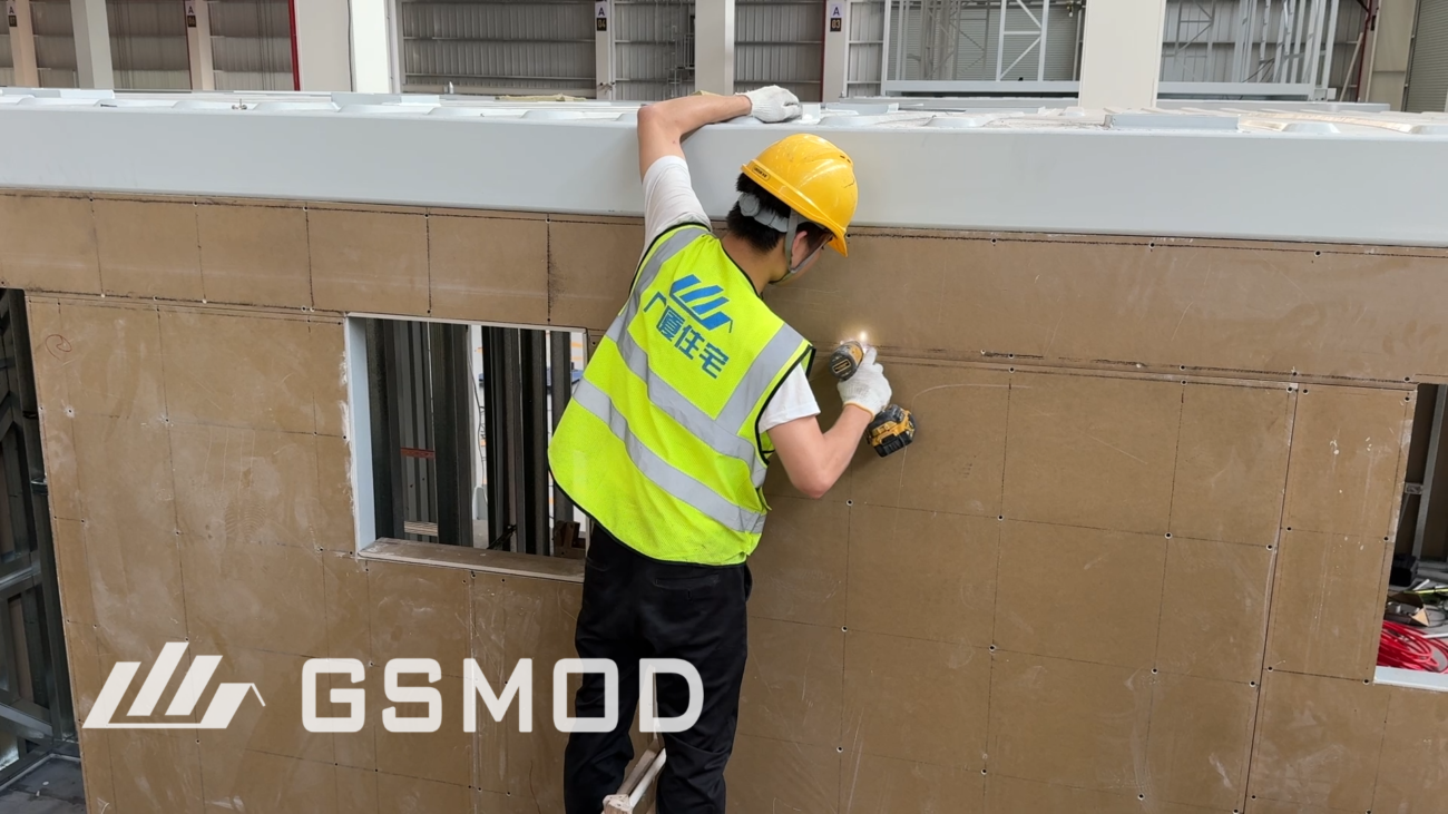 Worker installing wall sheathing panels on a prefabricated modular building in the factory